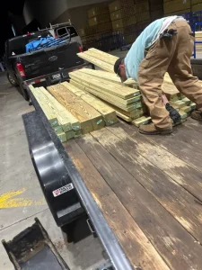 Male in his 30s expertly moves huge pieces of 2x4s on top of a truck.
