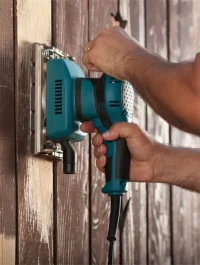 Man hands polishing old fence with power tool.